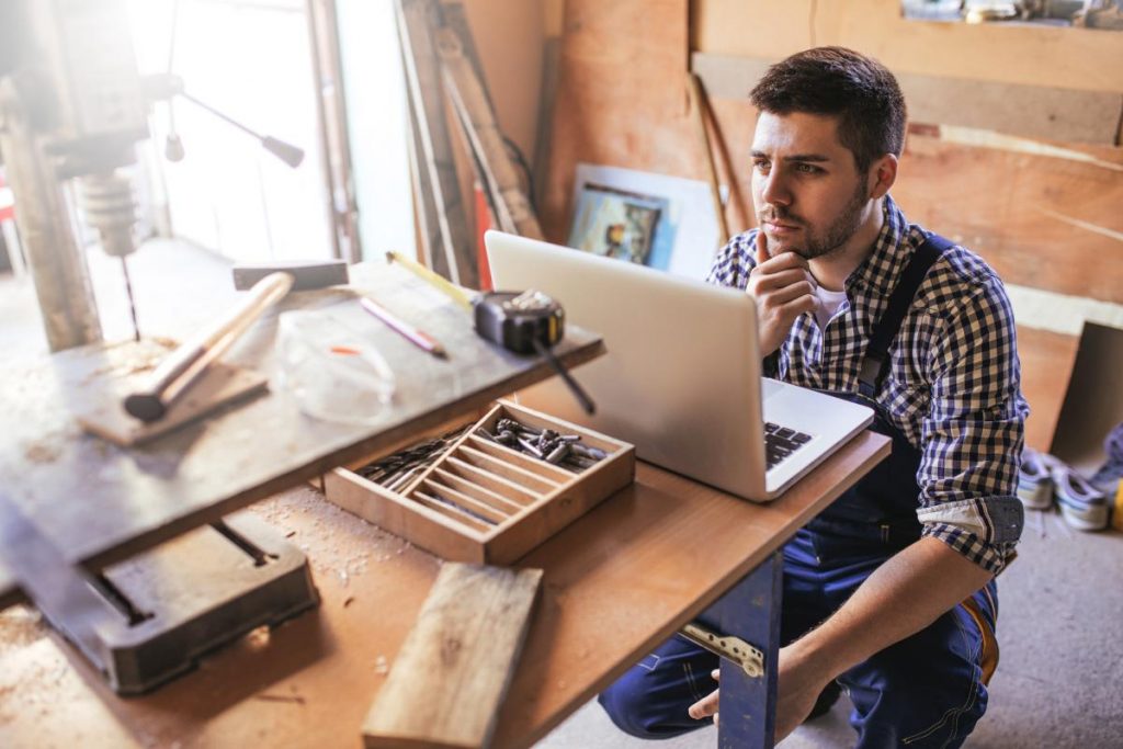 man in woodworking shop looking over laptop